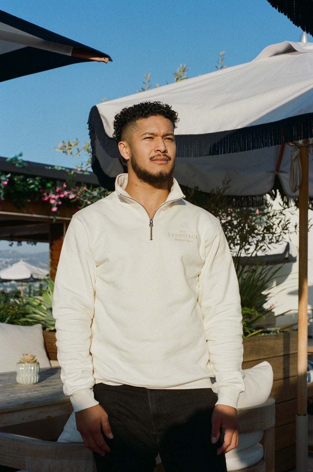 Man wearing the L'Ermitage Beverly Hills x Dinner Service NY limited merch half zip. 